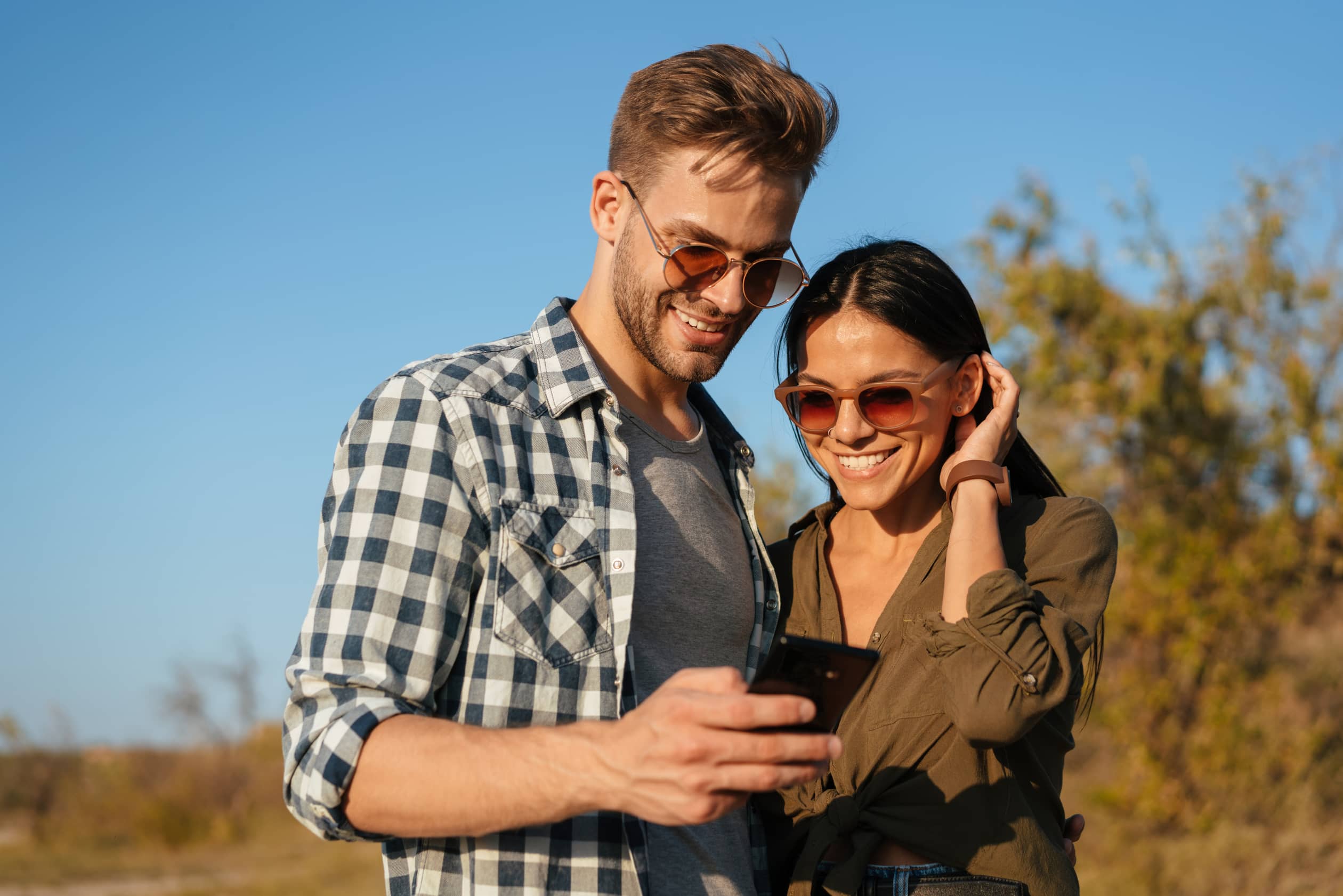 joyful couple hugging and using cellphone while strolling on nature